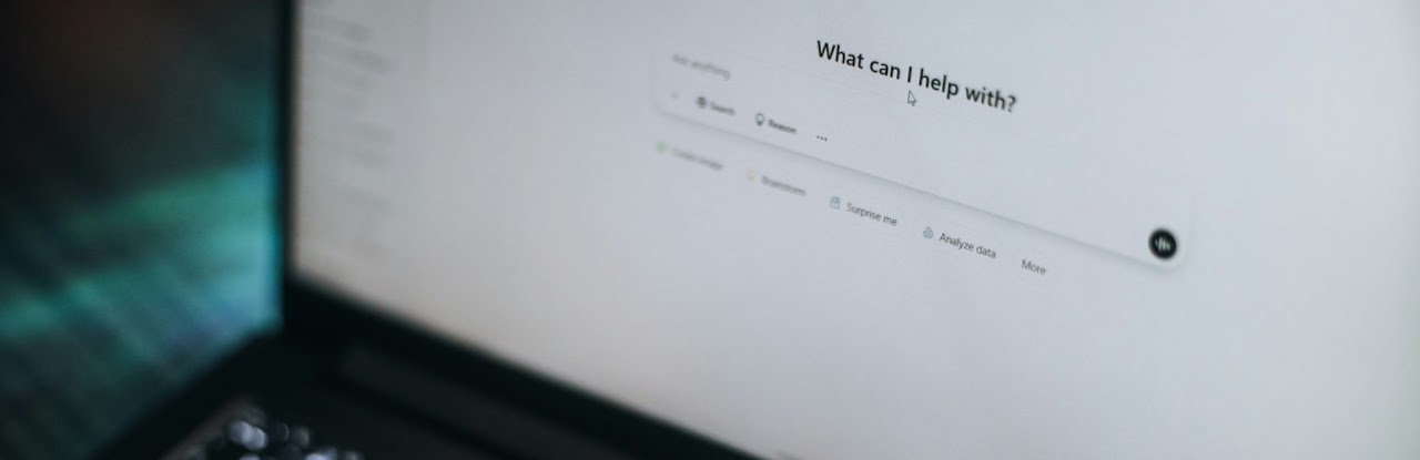 A laptop screen showing an AI assistant prompt reading 'What can I help with?' with quick actions for Search, Reason, Brainstorm and Analyze data