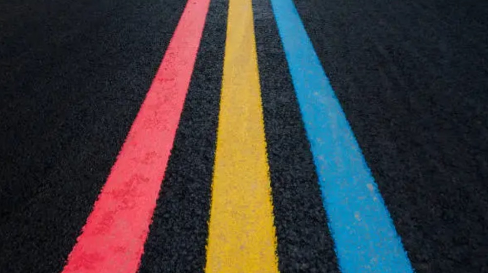 Three parallel painted lanes on dark asphalt, red, yellow and blue, running away into the distance
